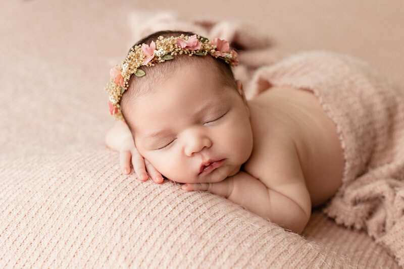 Newborn baby girl with hands on face laying on a pink background