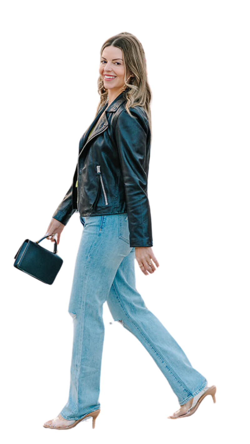 Solo woman smiling at the camera while wearing a stylish leather jacket and jeans, holding a handbag near the Louvre and Pont des Arts during a Paris solo photoshoot.