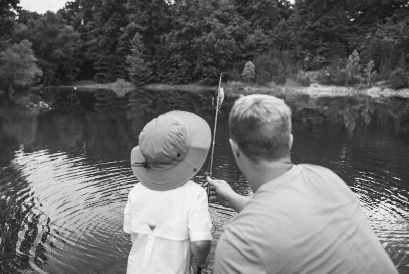 Black and white portrait taken behind father and son with their fishing pole and caught fish in the background. 
