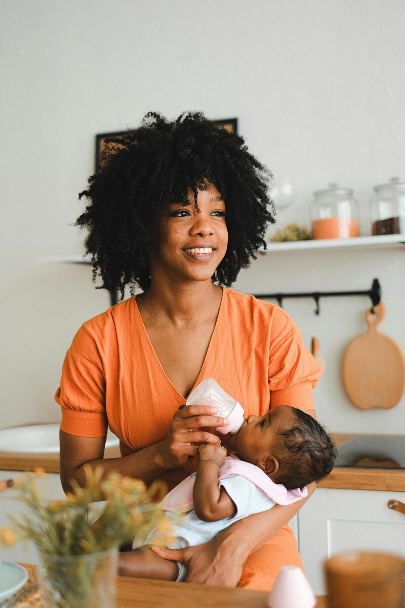 Woman bottle feeding her baby in a kitchen