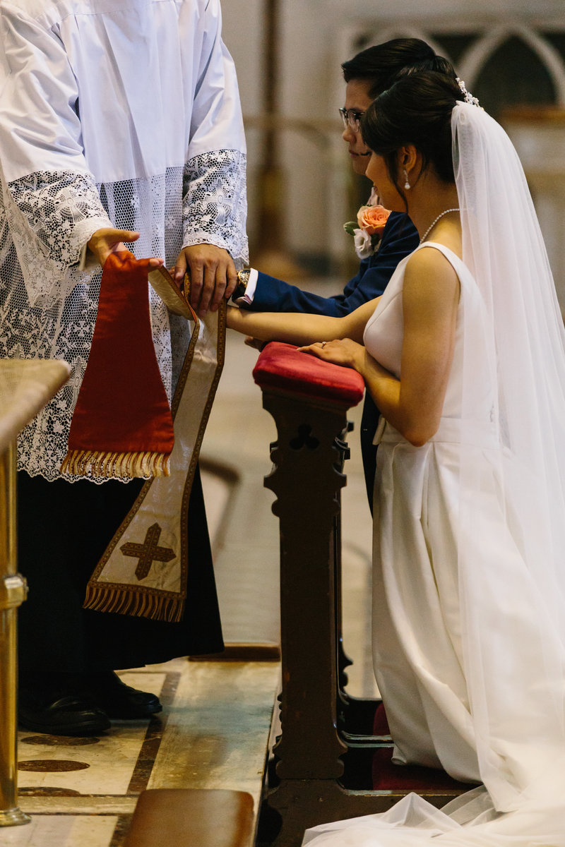 Bride and groom kneeling in front of priest during ceremony