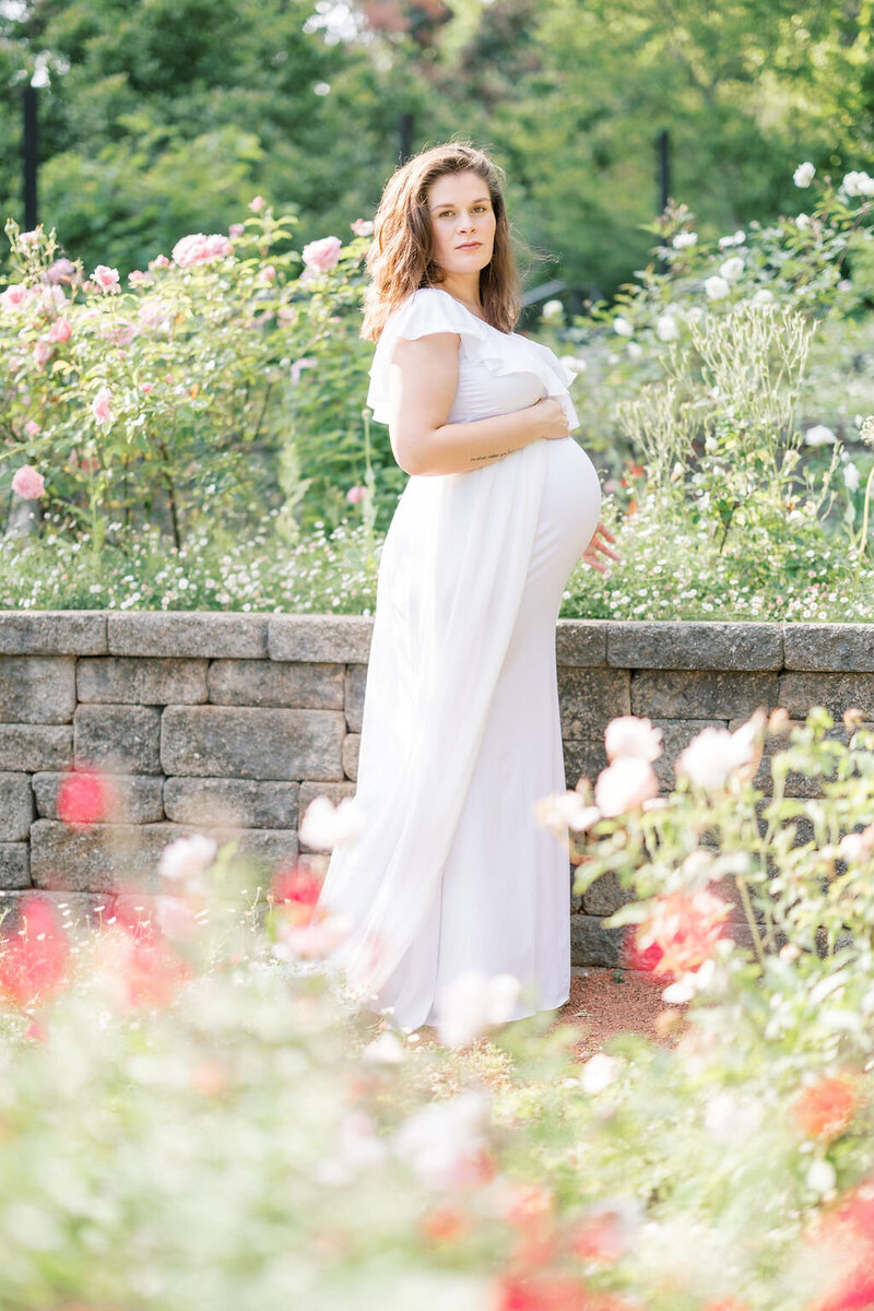 Woman in white dress holds baby bump in Athens botanical gardens