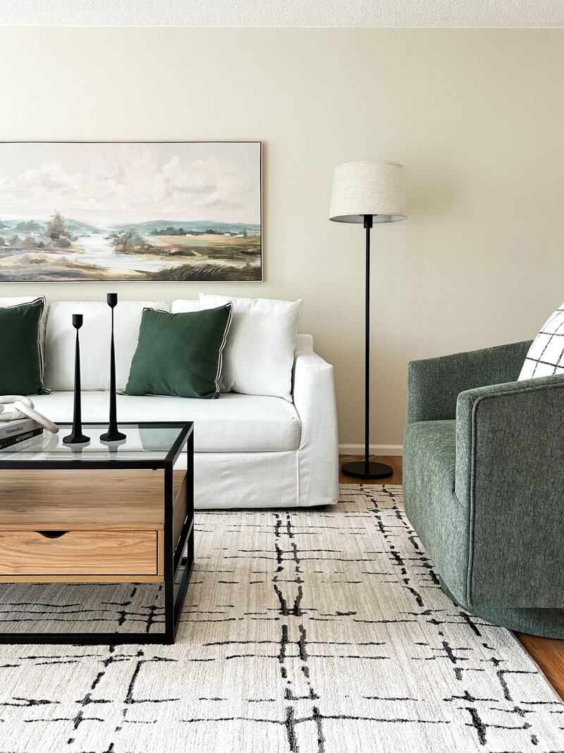 Family room staged by Modern Mollusk in Snohomish County featuring a white sofa, green armchair, modern artwork, and neutral decor.