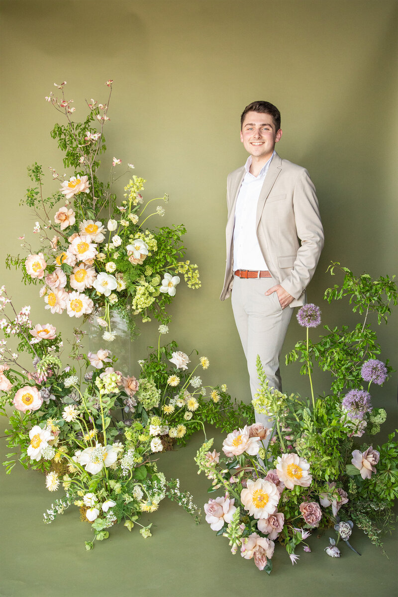Cole Buys standing with flowers in background.