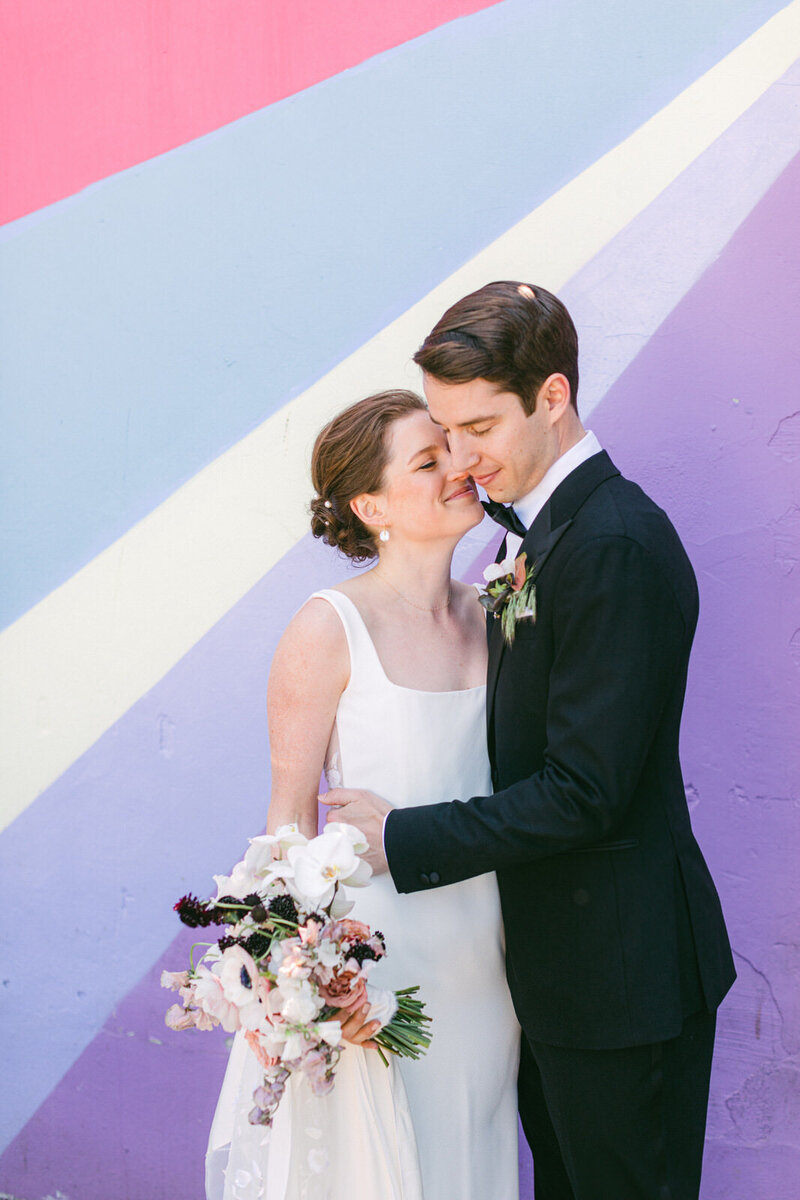 bride and groom embrace in front of a colourful painted wall