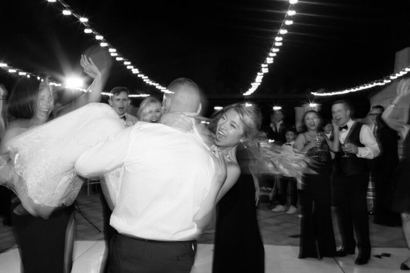 wedding couple dancing during reception groom has lifted up bride and is spinning her around. she is laughing.