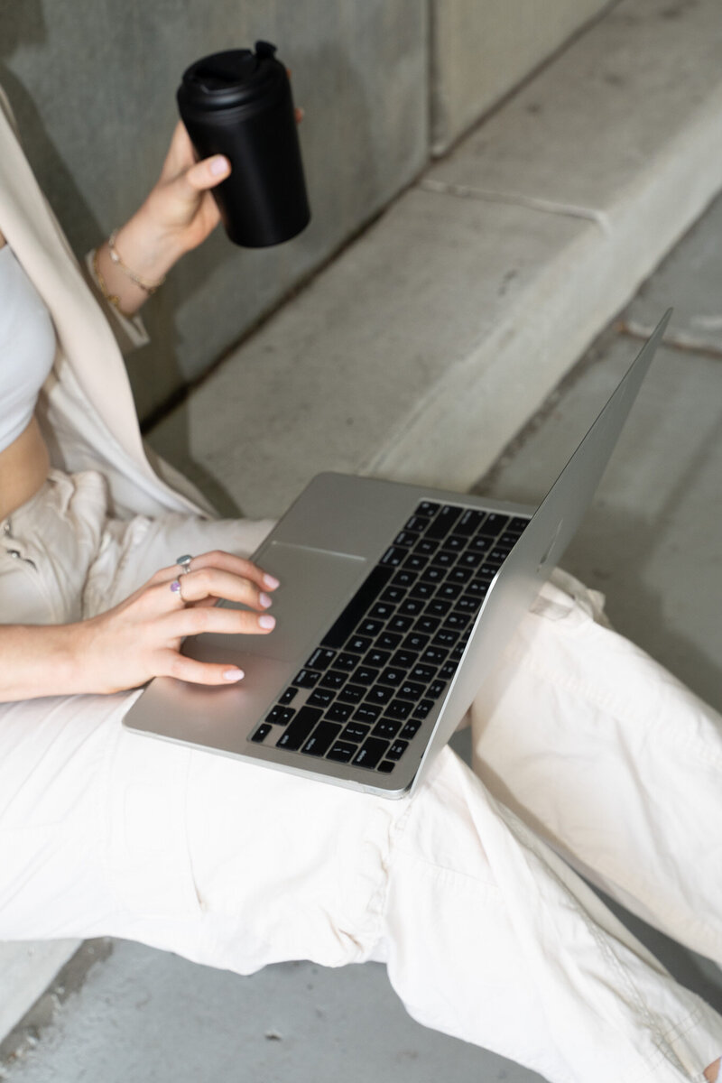 Entrepreneur sitting on stairs with laptop and to-go coffee cup
