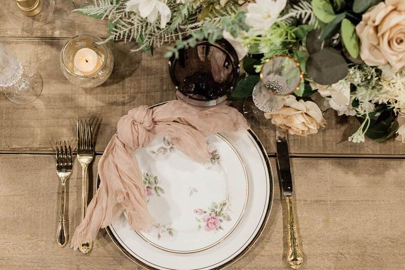 Reception dinner place setting and florals on a wood table at The Rosewood Venue.