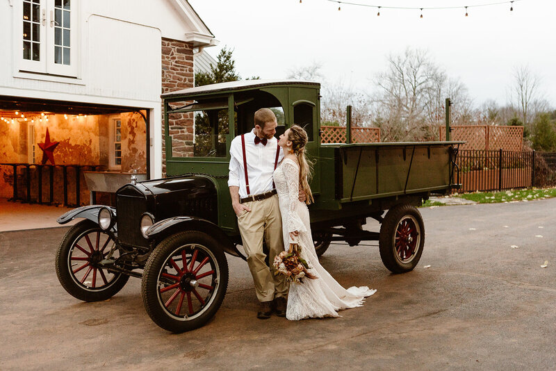 Couple lean against vintage car during their Pennsylvania farm wedding.