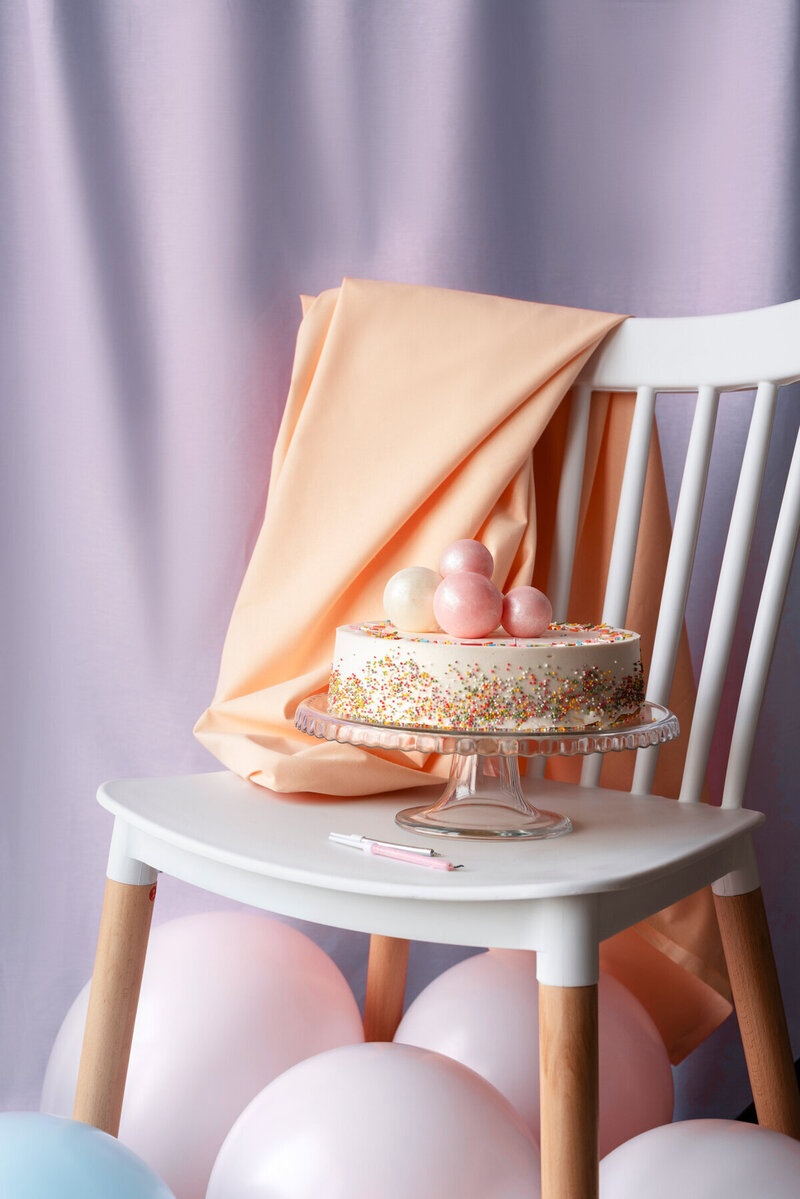 Gâteau recouvert de confettis et de boules roses posé sur une chaise pour l'organisation de baby shower.