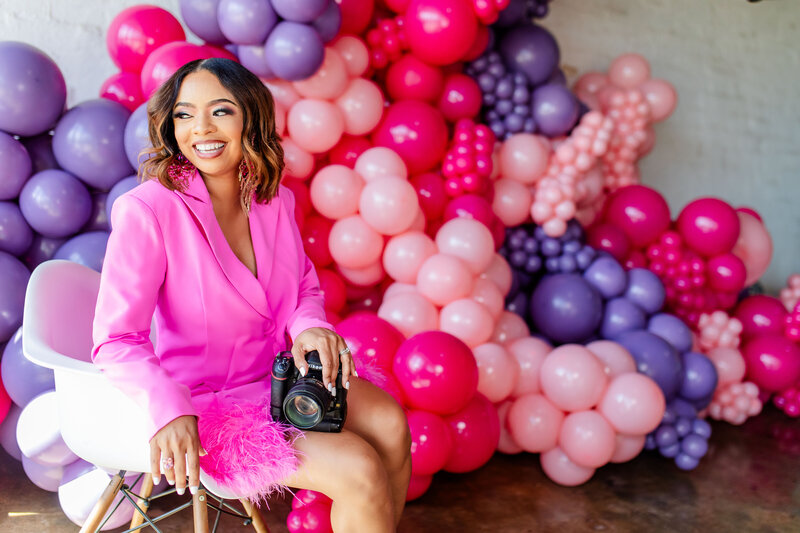 Capture the moment! Tiffany of Sunshine Images, this vibrant image radiates creativity and happiness. A joyful Black woman laughs while holding her Nikon camera in front of a stunning balloon installation by Popout Decor.