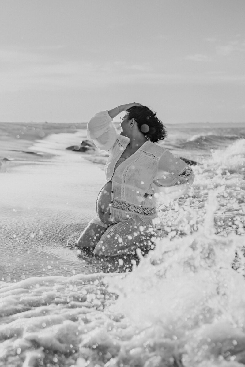 Pregnant mom sitting by the ocean with waves crashing around her