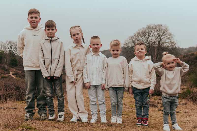 Een groep kinderen in witte kleding staat in een veld, omringd door groen gras en een heldere lucht.