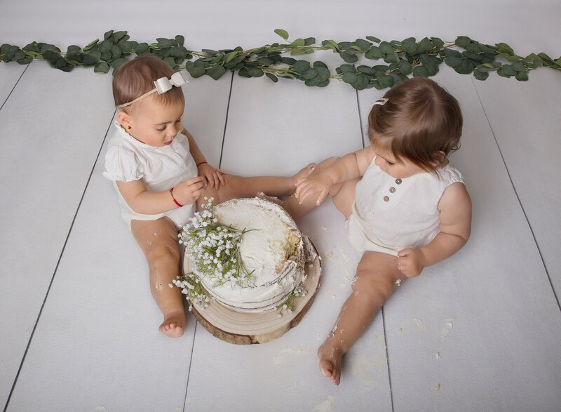 Aerial image of cake smash photoshoot. Baby girl and boy wearing white are captured playing with cake. Captured by best Brooklyn, NY cake smash photographer Chaya Bornstein.