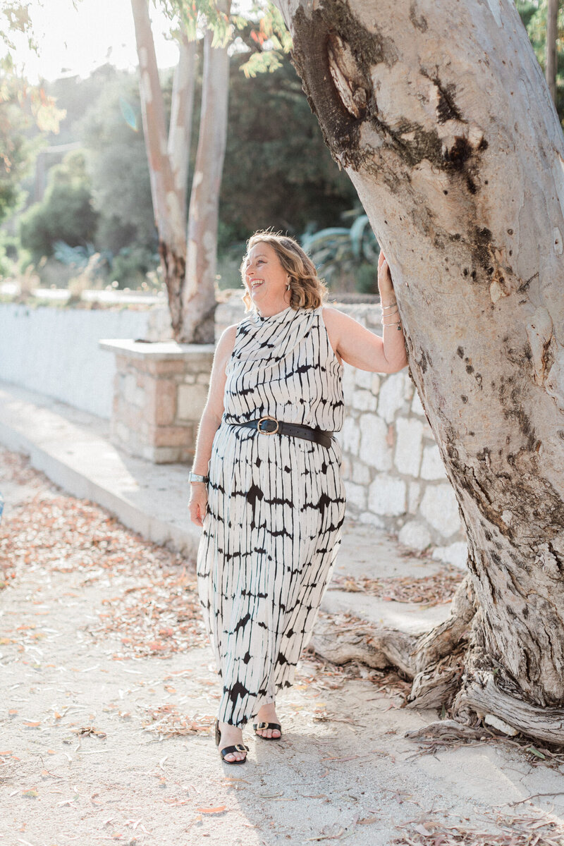 Portrait of Susan White, Ionian Islands wedding planner, standing by a sunlit tree in Greece.