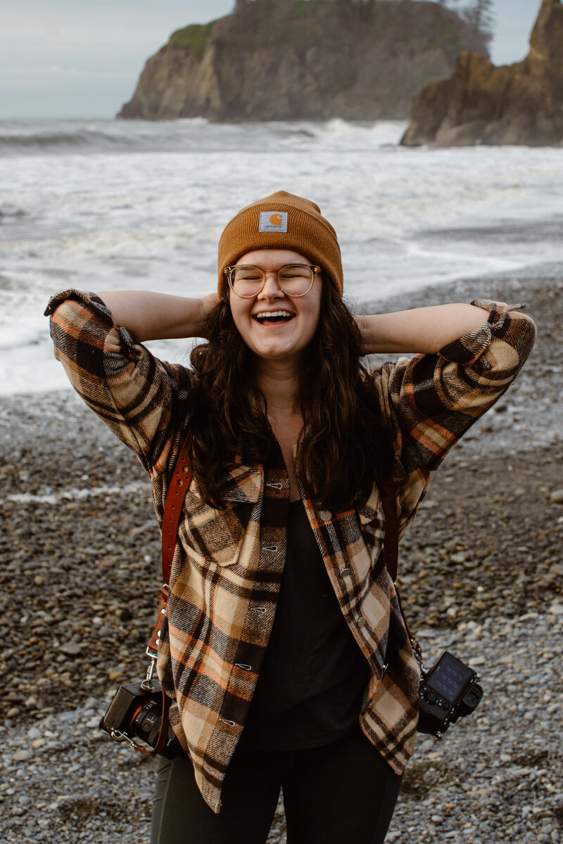 Janelle Renee, Washington elopement photographer, posing with cameras on Ruby Beach