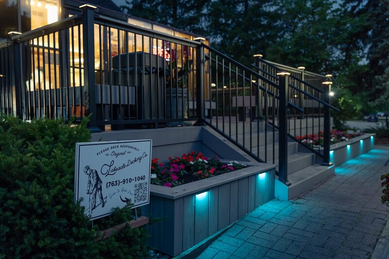 Low-maintenance deck with built-in planters on ground level with integrated LED lights, shining at night in the color teal. 