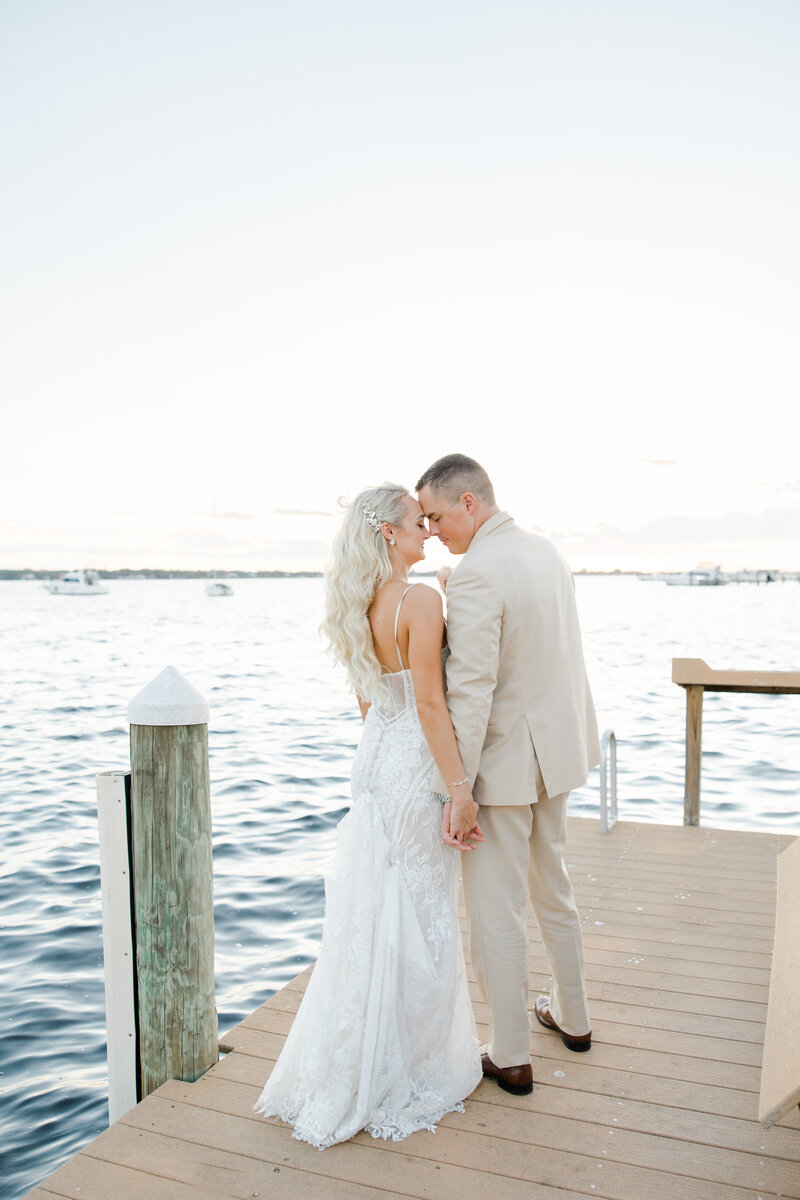 bride and groom holding hands on a dock at sunset