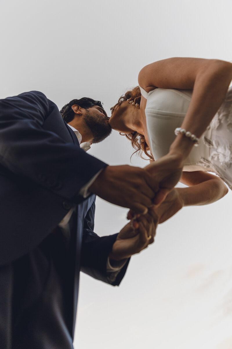 Wedding couple kissing and holding hands from a low angle during their ceremony