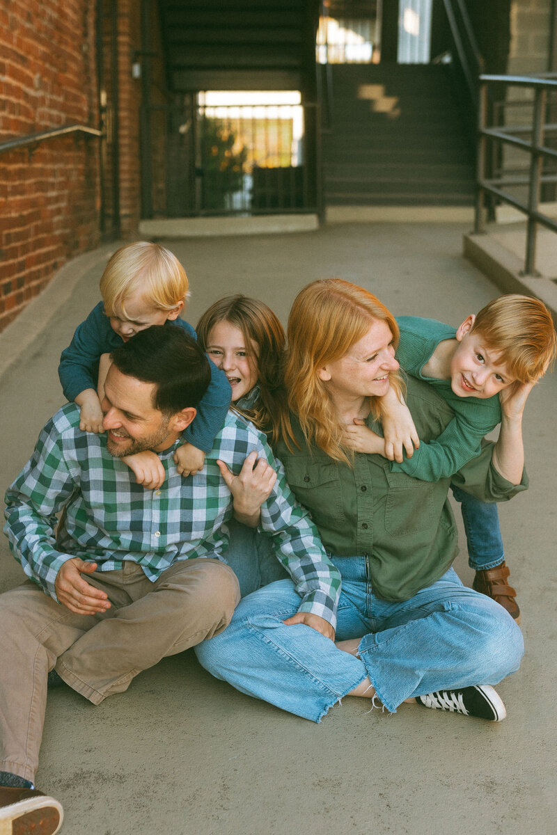 A family of five sitting on the ground holding each other and laughing.