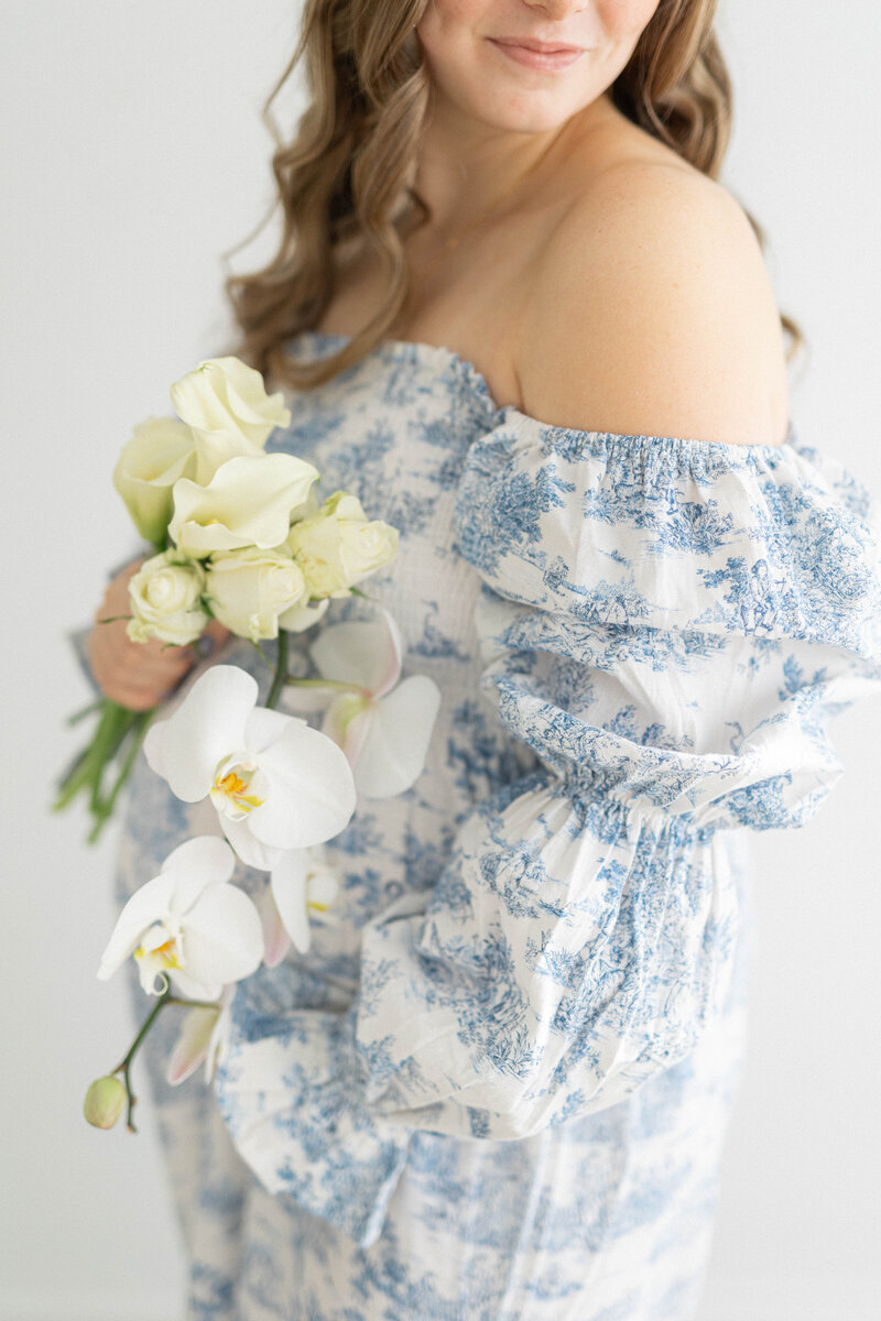 knoxville mom in blue and white dress holding flowers and dress in a studio