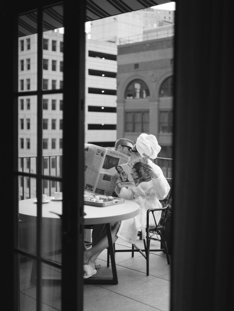 couple in bathrobes, bride in head towel, read magazines & newspaper, share brunch on Shinola Hotel Detroit balcony, engagement session