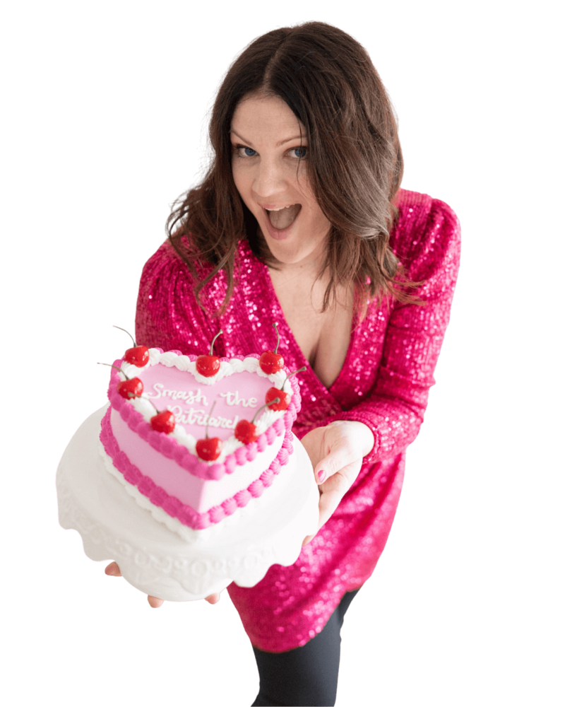Emily, wearing a pink dress, holding a cake that says "smash the patriarchy."