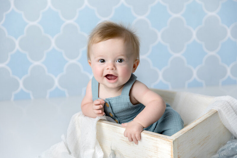 6 month old boy smiles for a milestone studio portrait on a blue background