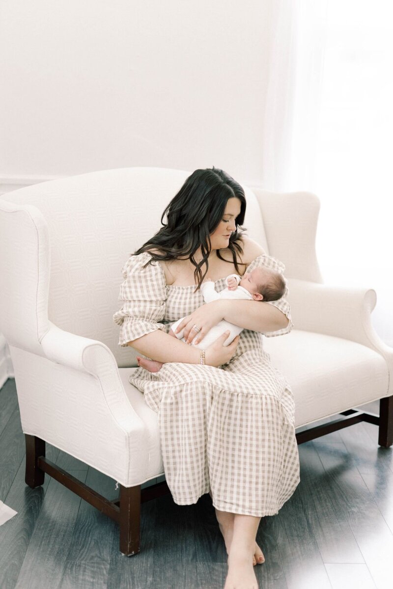 Mother sits on white chair holdings newborn baby.