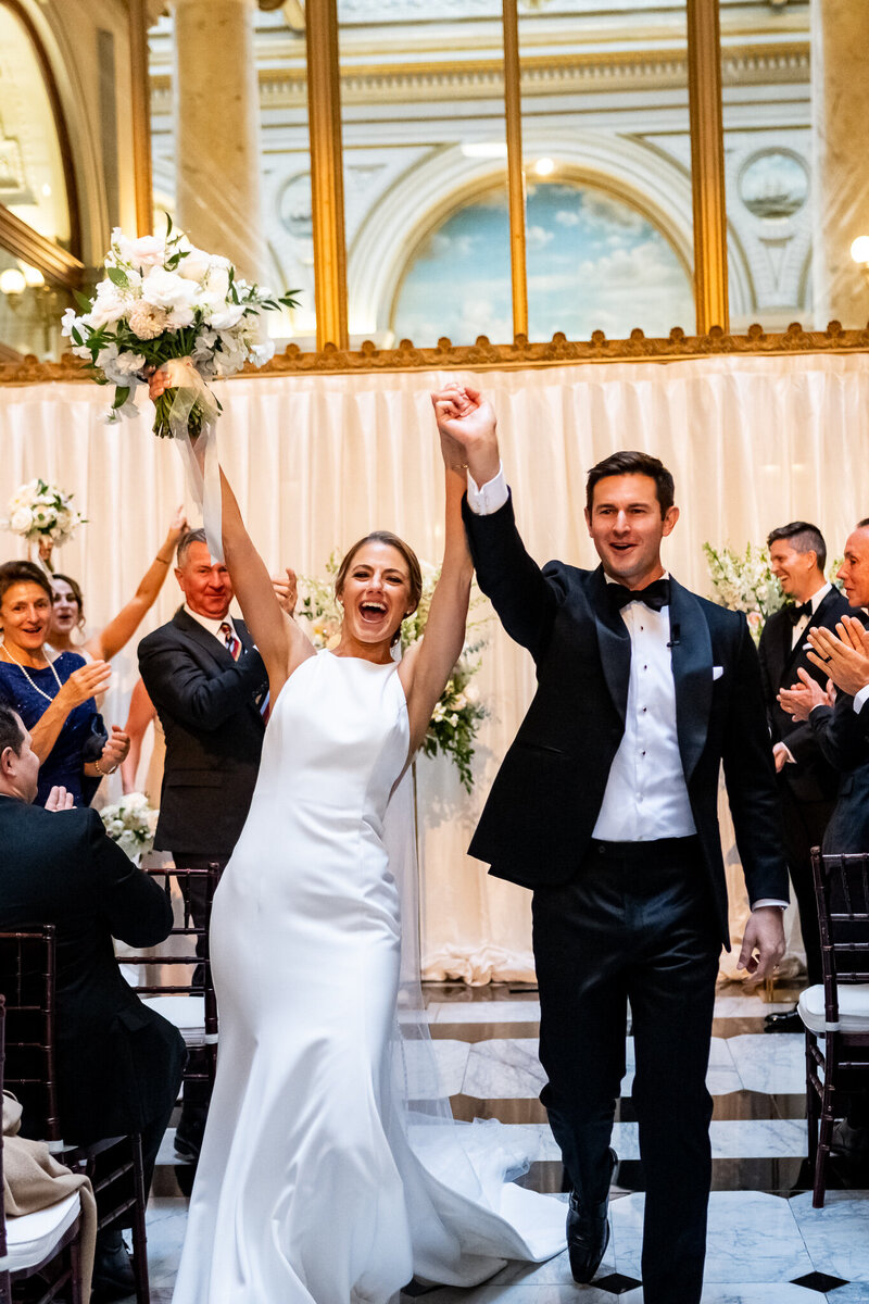 San Francisco wedding photographer captures celebratory recessional of the bride and groom at the  Merchants Exchange Building Lobby for their Julia Morgan Ballroom