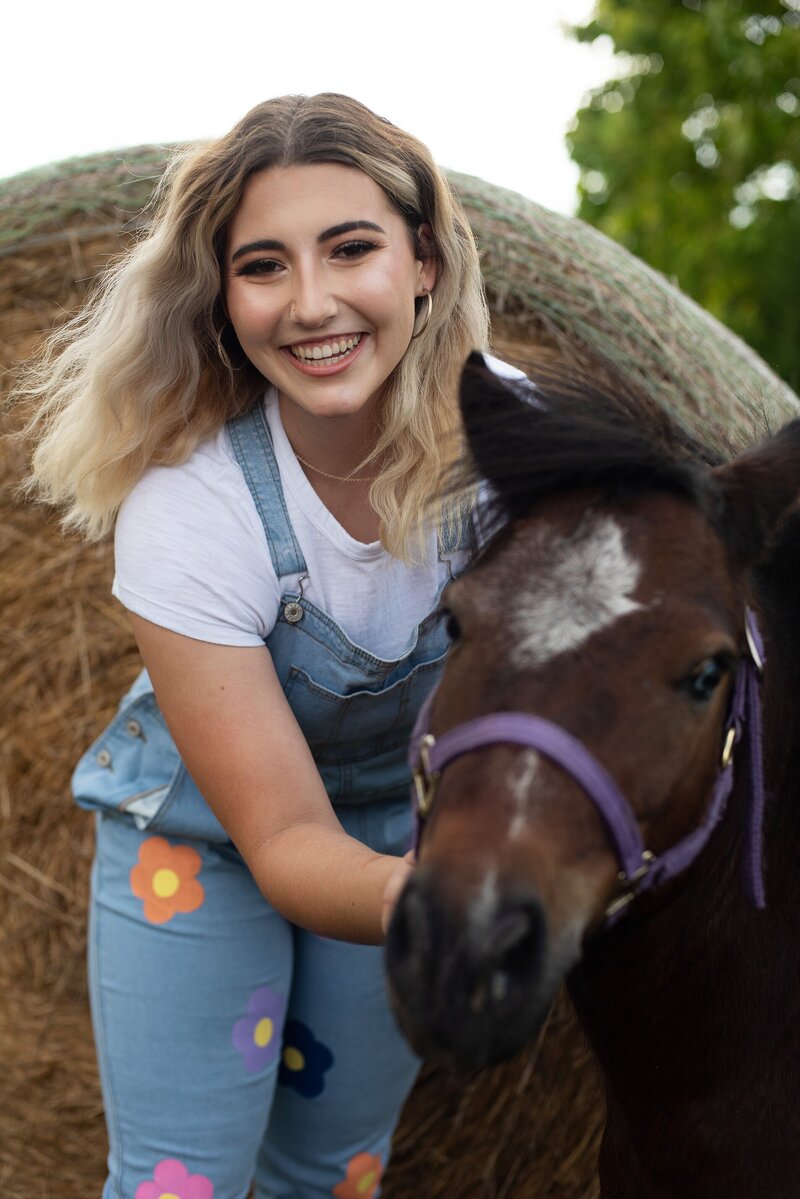 high school senior pictures farm themed shoot girls dreessed in ovralls posing with red tractor