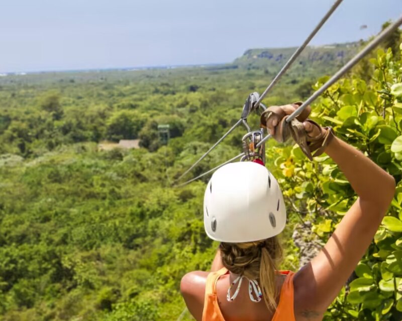 Back view of a woman ziplining over lush green forest in the Dominican Republic