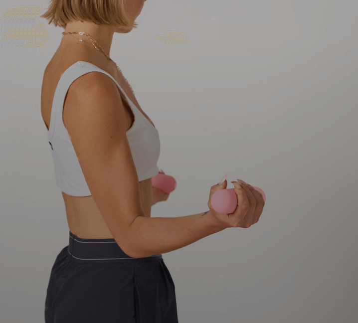 Women in a white workout top and black pants holding Bala hand weights in her arms 