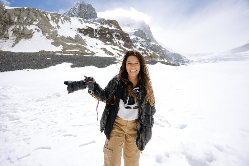 Wedding photographer in the Canadian Rockies holding a camera on a snowy mountain, showcasing professional Canmore and Banff photography services.