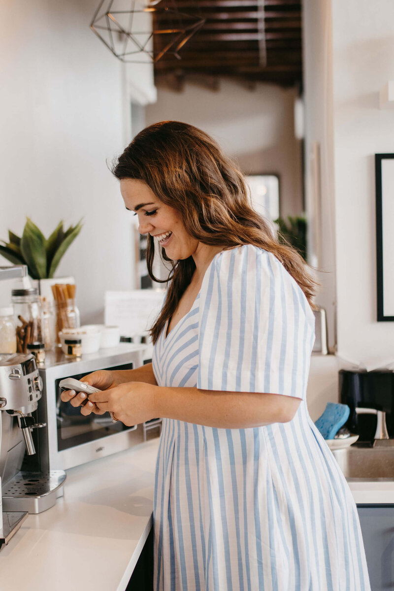 woman with dark hair on cellphone making coffee in white and blue striped dress