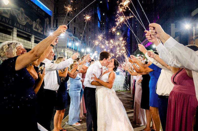 Bride and groom kissing outside of the Lucy in Philadelphia while their guests hold up sparklers over them