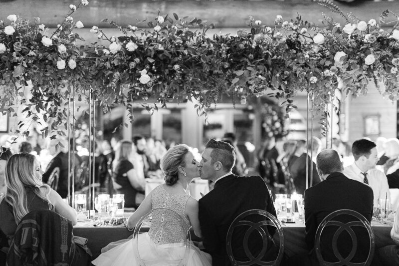 Les mariés s'embrassent lors de la réceptipn de mariage, sous les fleurs de la décoration.