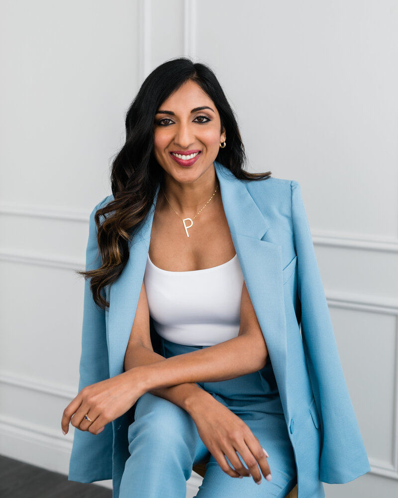 Priya Sam, Keynote Speaker and Toronto Podcast Host poses in a blue suit and white top.