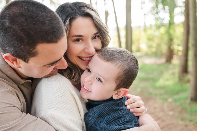 mom and dad hugging their little boy while mom is smiling at the camera by lancaster pa photographer