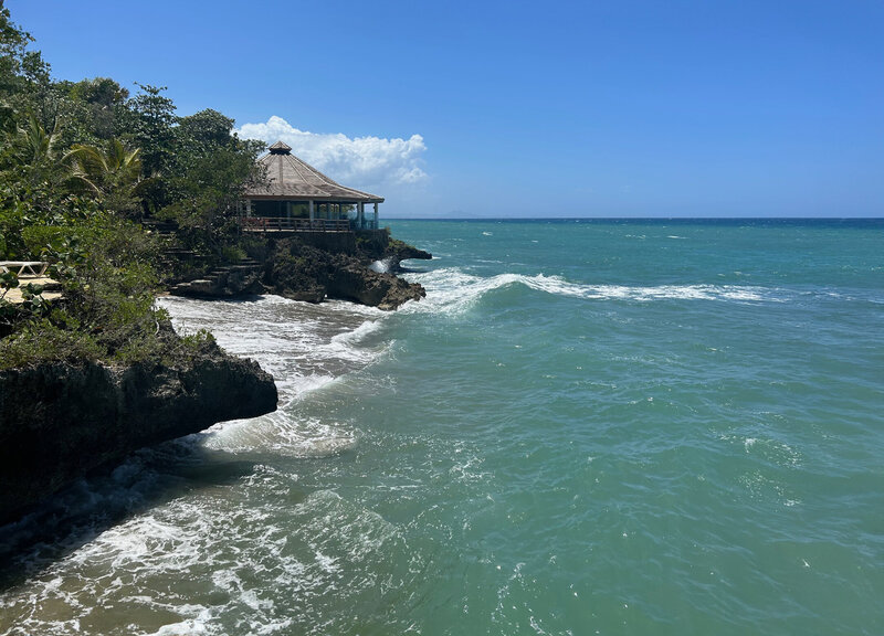 Thatched-roof gazebo perched on the edge of a cliff by turquoise waters