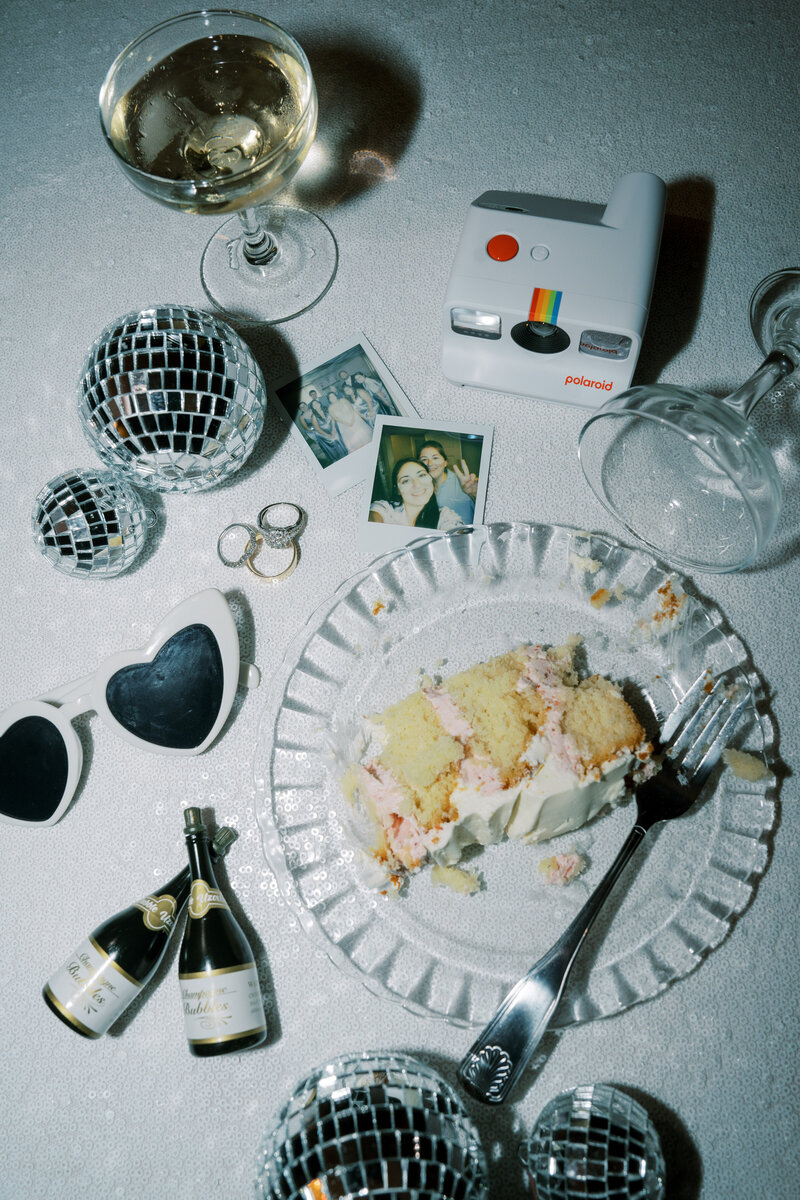 Flash photo of late night wedding details including cake, polaroids, disco balls, and wine glasses