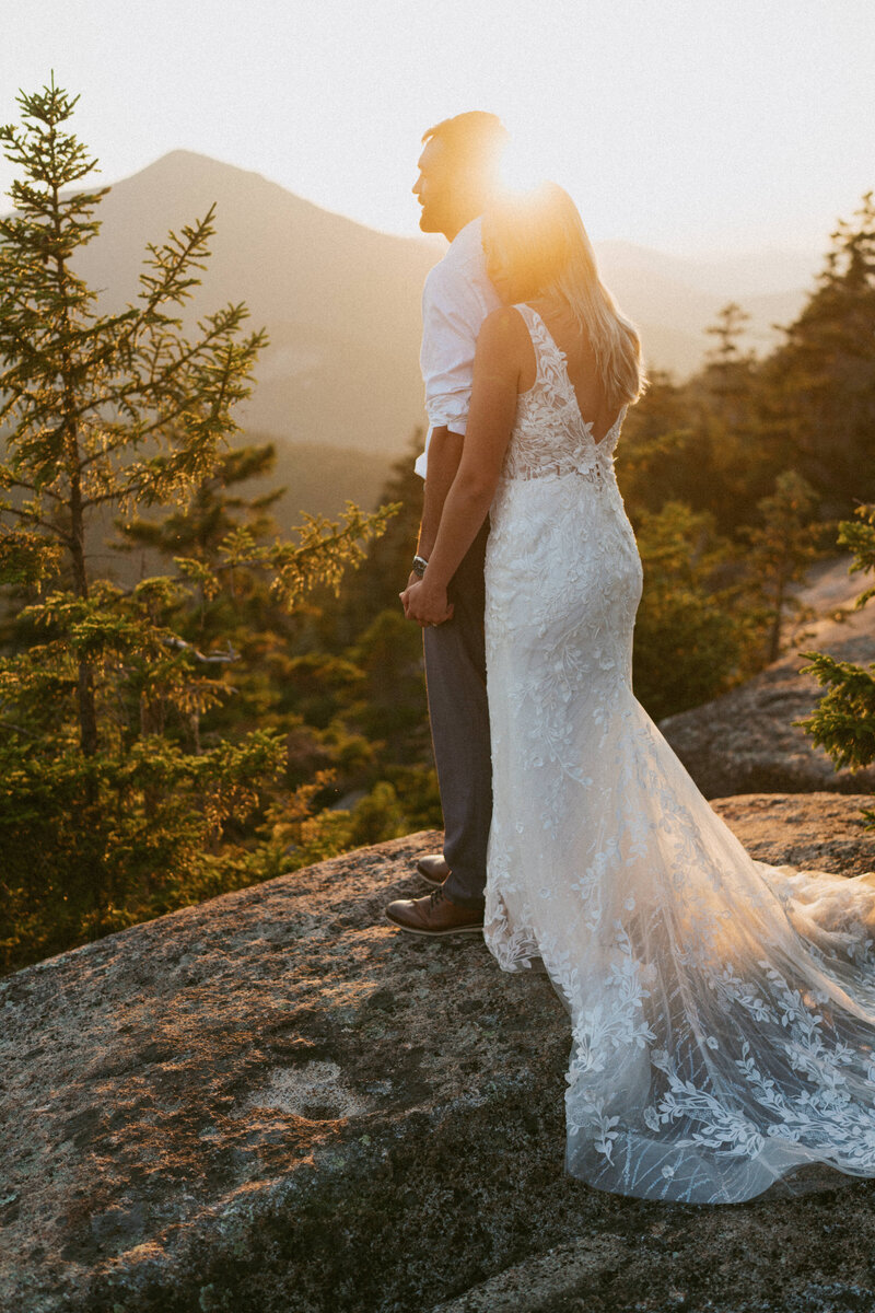an elopement couple snuggling together on the top of a mountain in New Hampshire during their elopement as the sun sets in the background