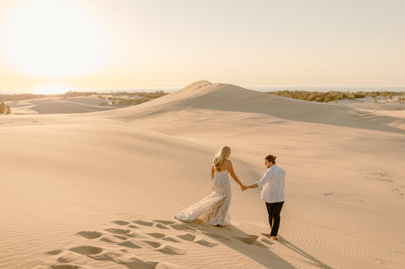 couple holding hands running through sand dune