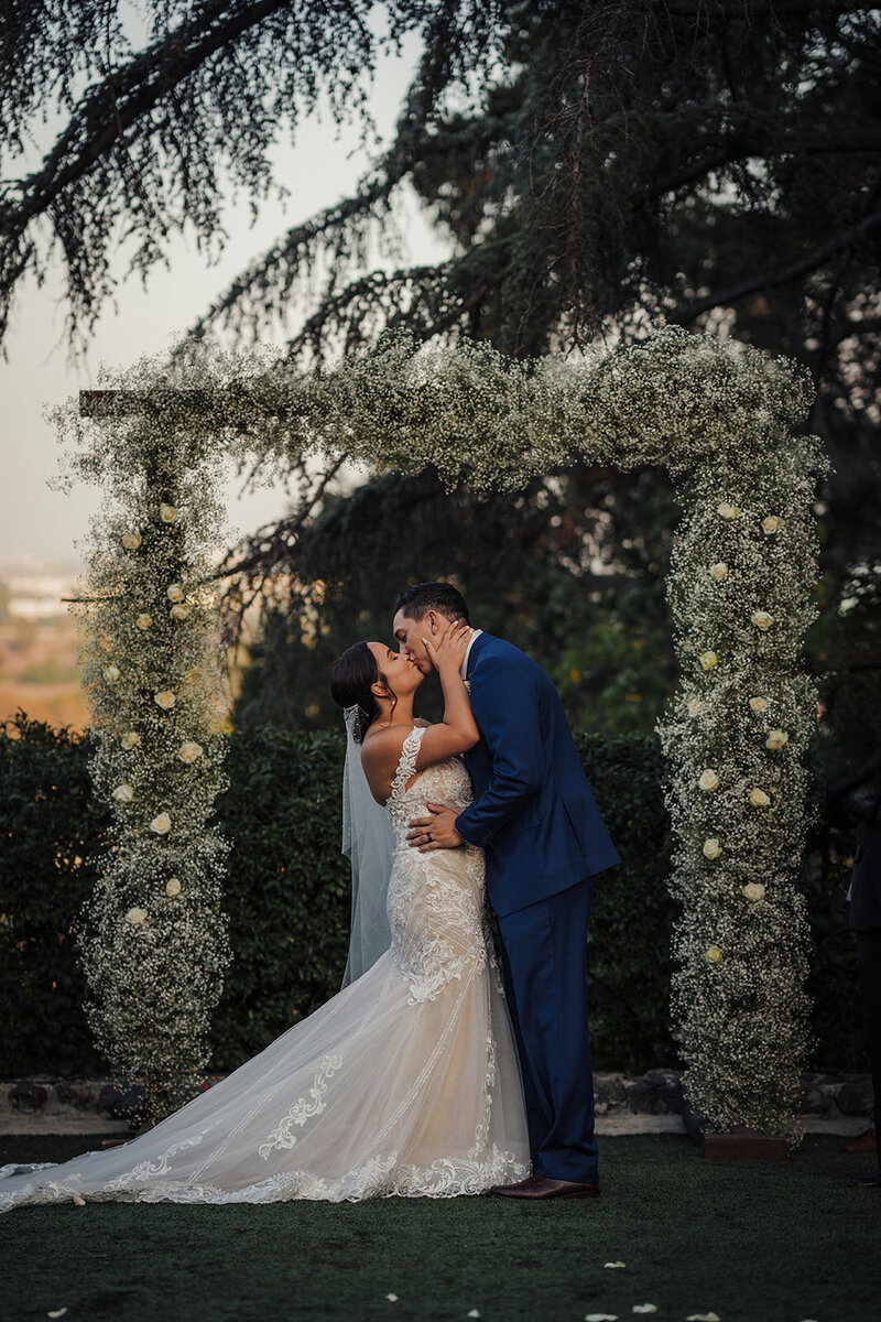 Bride and Groom have their first kiss under a floral arch at the Kellogg House in Pomona, California
