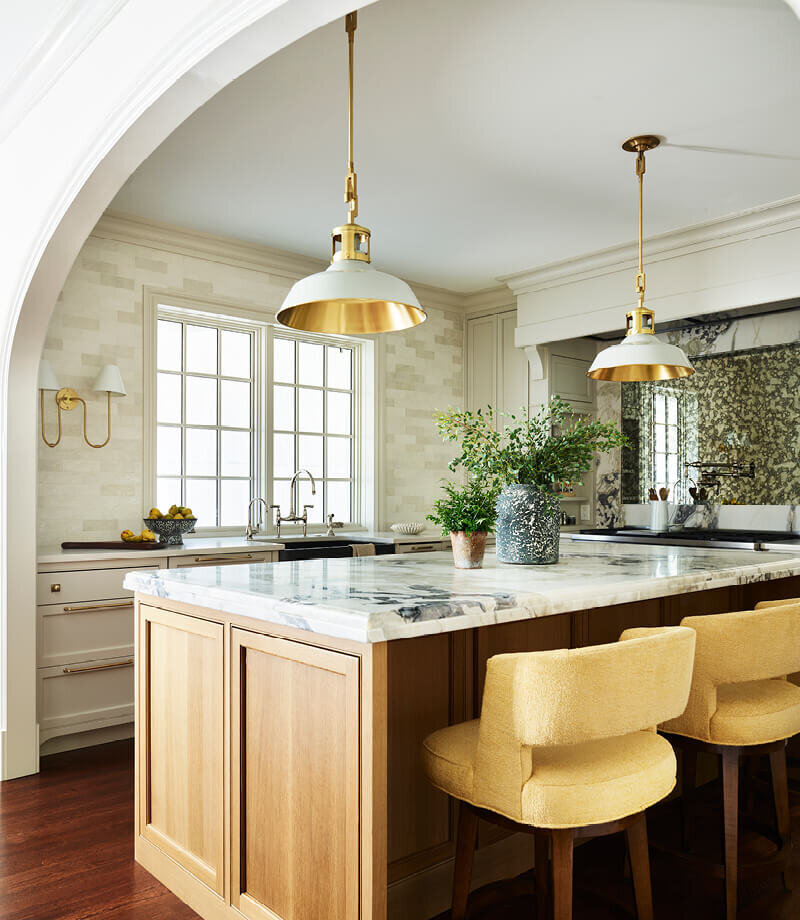 A traditional kitchen design in Milton featuring white kitchen cabinets, a natural oak island, custom yellow stools, and a brass light fixture for warmth and charm.