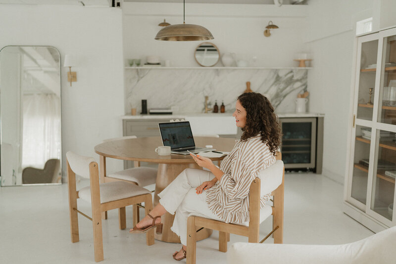 Morgan carrying a laptop and coffee cup by a table