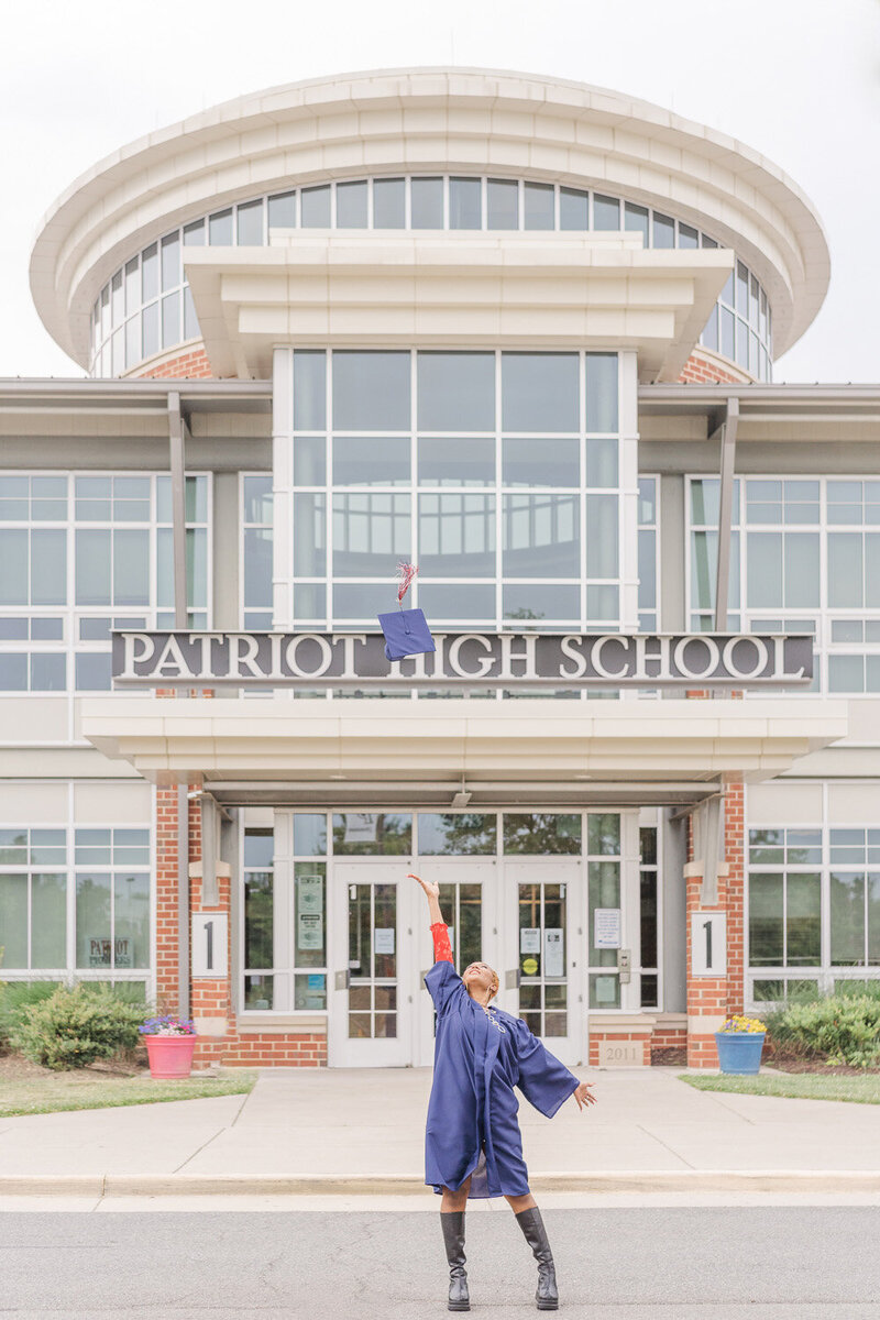 girl wearing graduation gown throwing cap outside her school  during senior pictures in Nokesville, VA