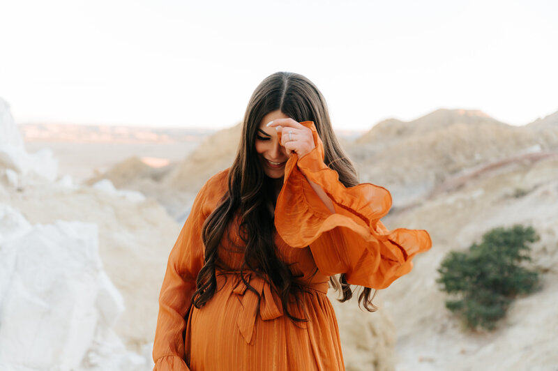 Woman in orange dress holding her face during her maternity session