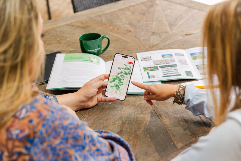details of women working on a wooden table seen from behind, one showing details on a phone to the other during branding photoshoot with Laure Photography Atlanta