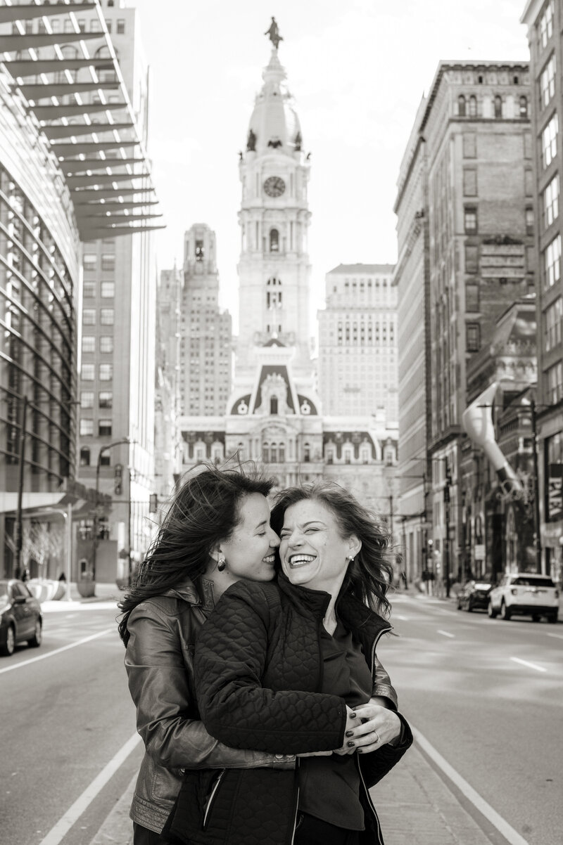A person standing behind their partner and leaning into them as they smile 